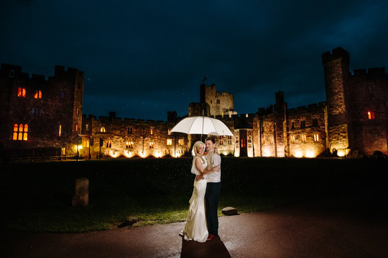 Bride and Groom under umbrella at night outside the castle