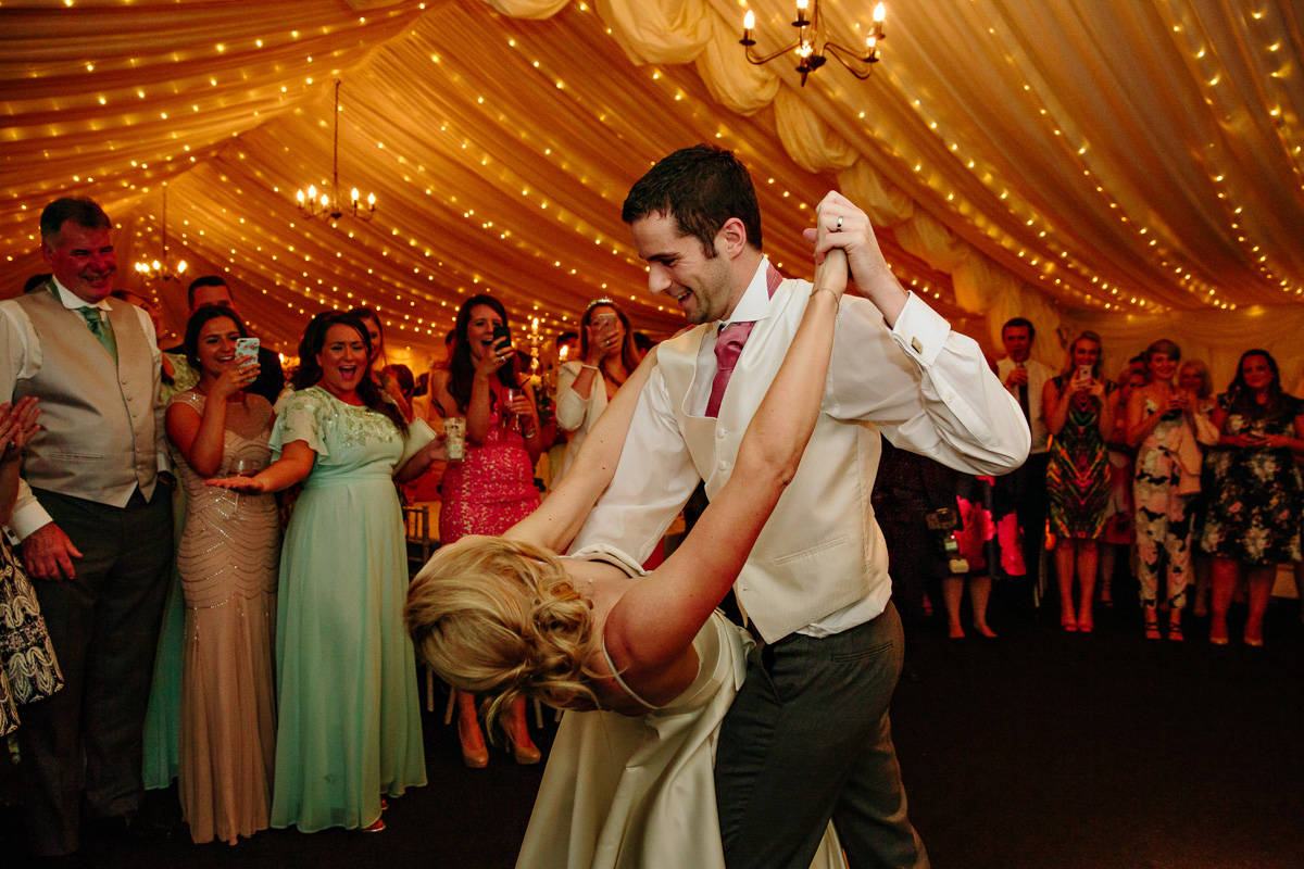 Groom dipping the bride during their first dance as all of the wedding guests watch on