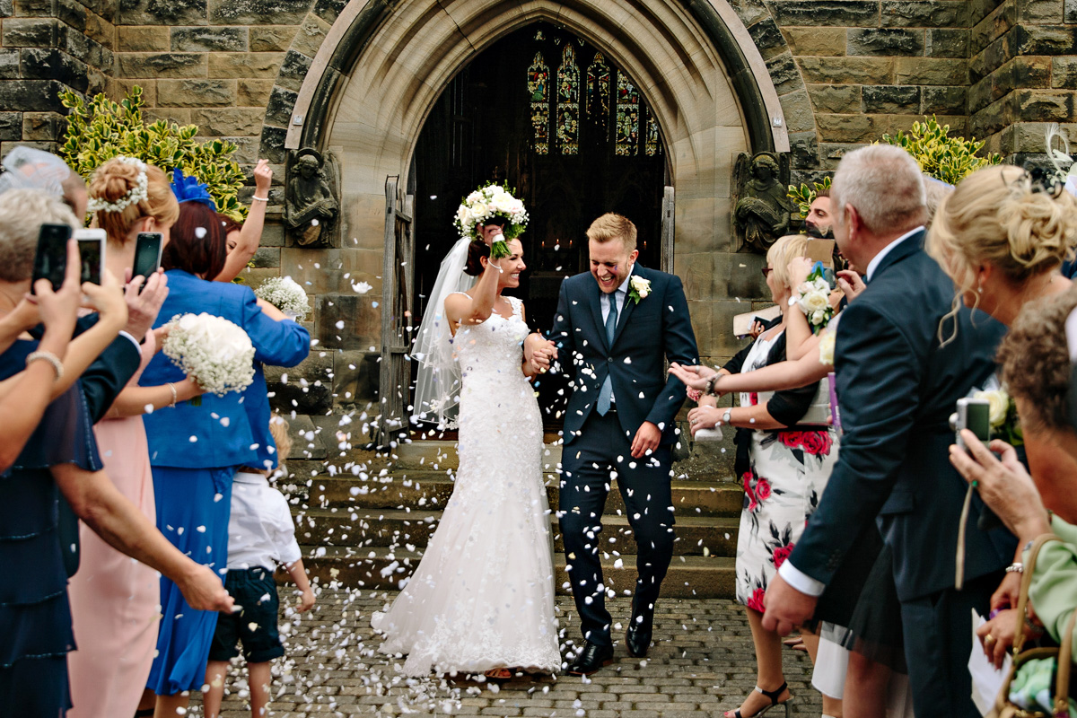 Bride and Groom leaving church getting showered with confetti by the wedding guests