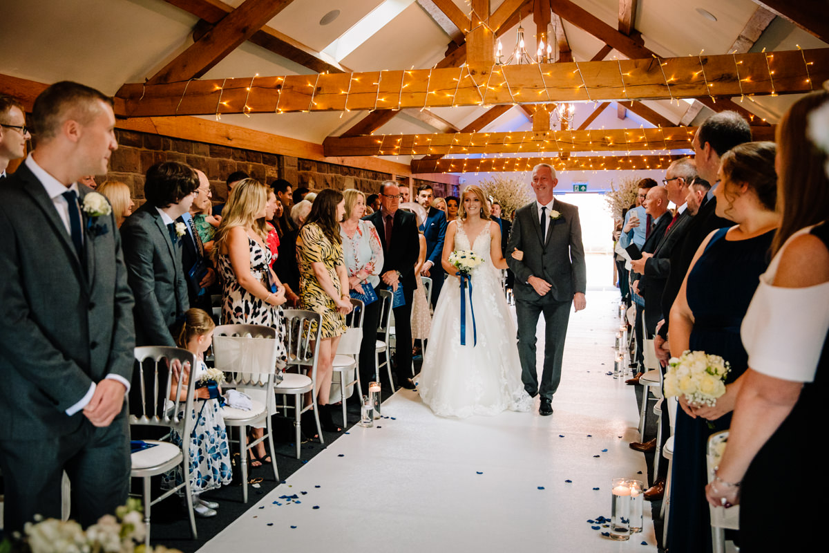 Bride walking down the aisle with her father in the rustic barn ceremony