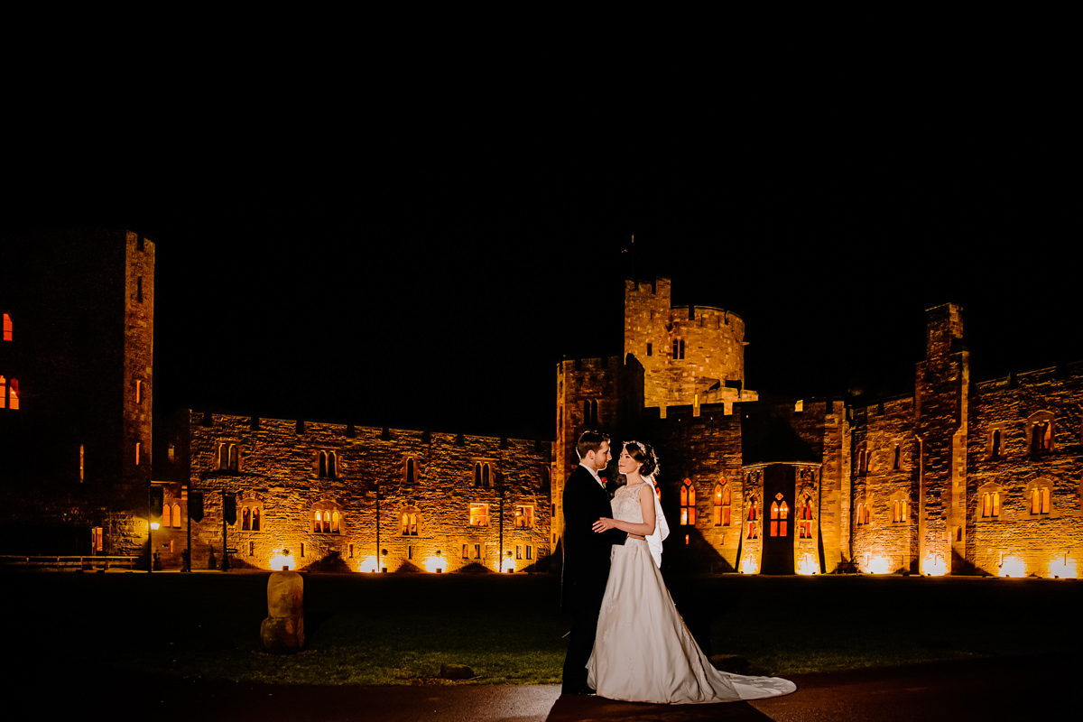 Peckforton Castle lit up in the evening with the bride and groom