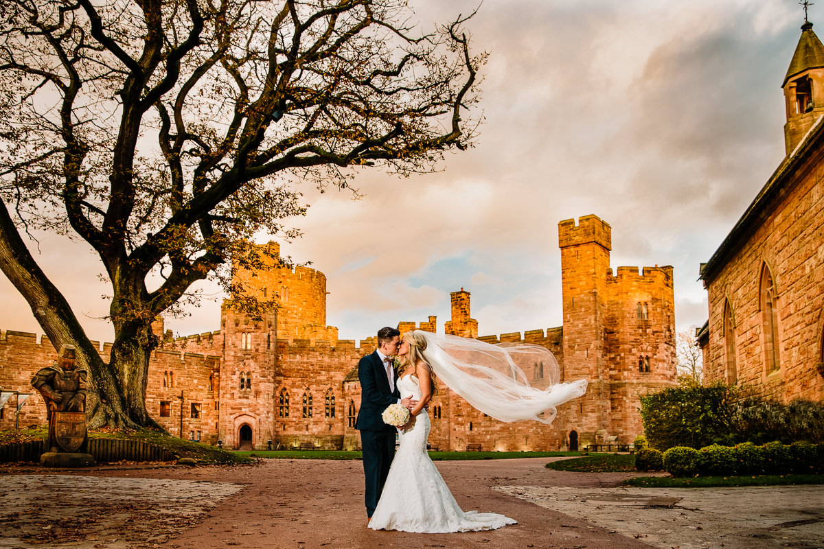 Peckforton Castle bride and groom loving moment together with the brides dress blowing in the wind