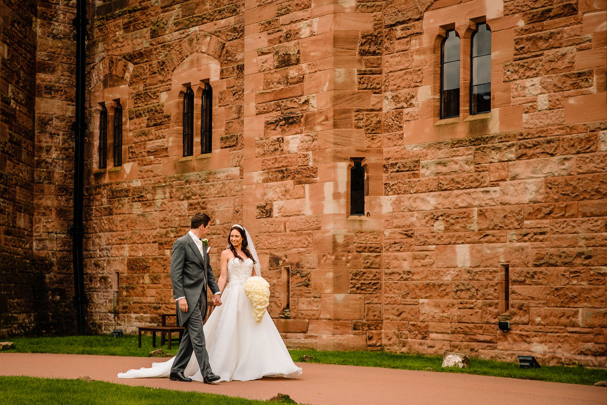 Bride and Groom walking hand in hand in the grounds of Peckforton Castle after just getting married