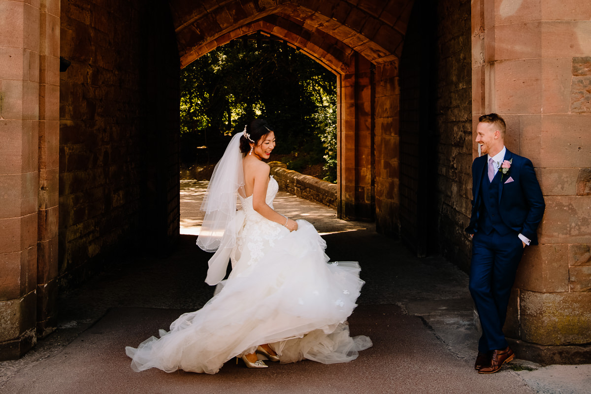 Bride swishing her wedding dress while the groom watches happily