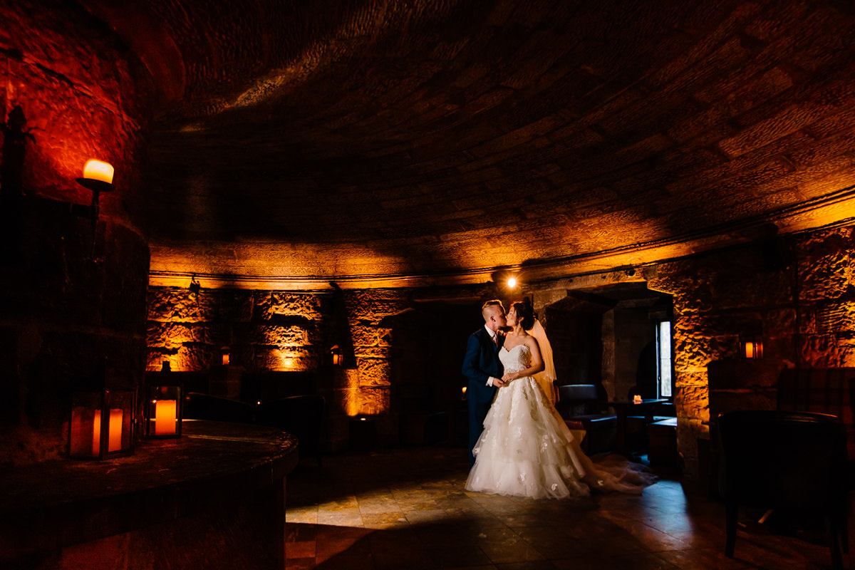 The wine cellar at Peckforton castle lit by candles with a bride and groom