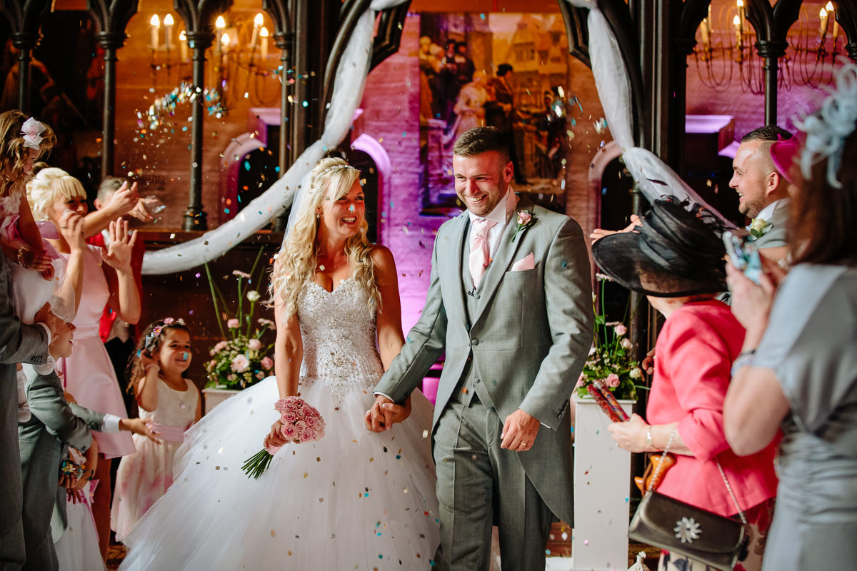 Bride and groom showered with confetti by their wedding guests as they walk down the aisle 