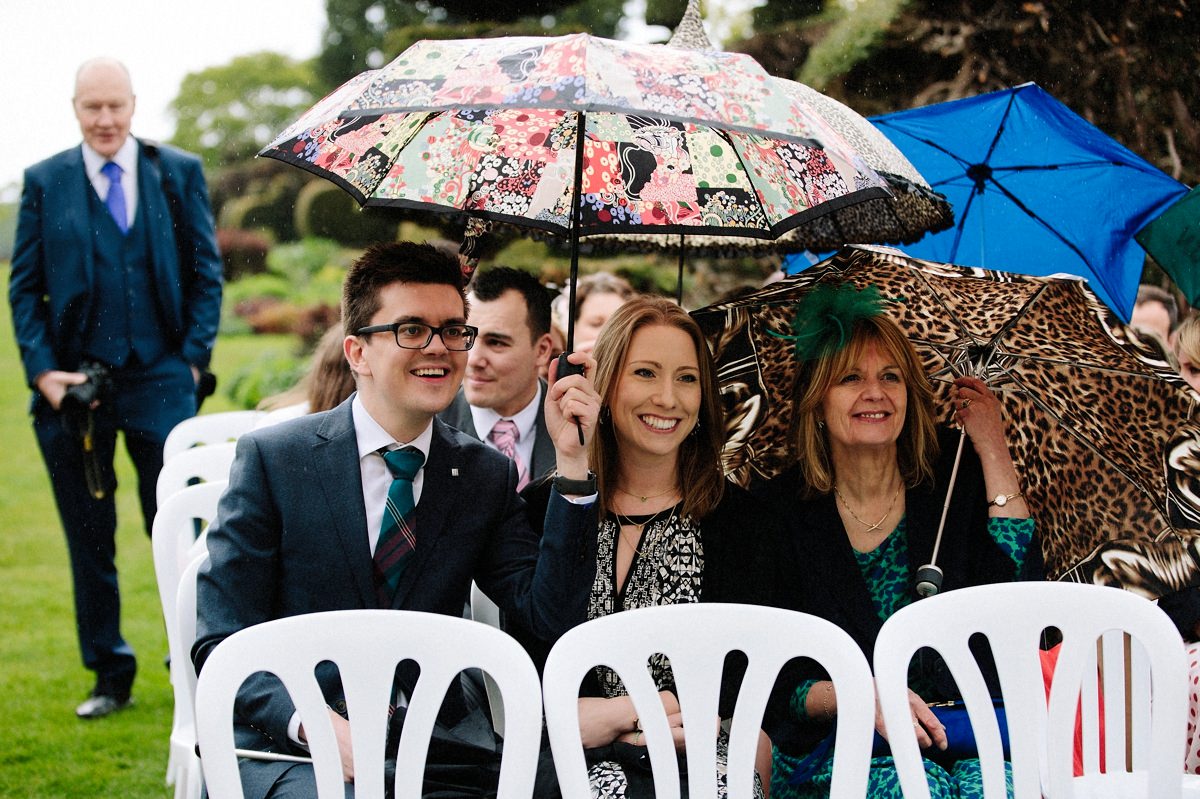 Wedding guests sheltering from the rain under umbrellas