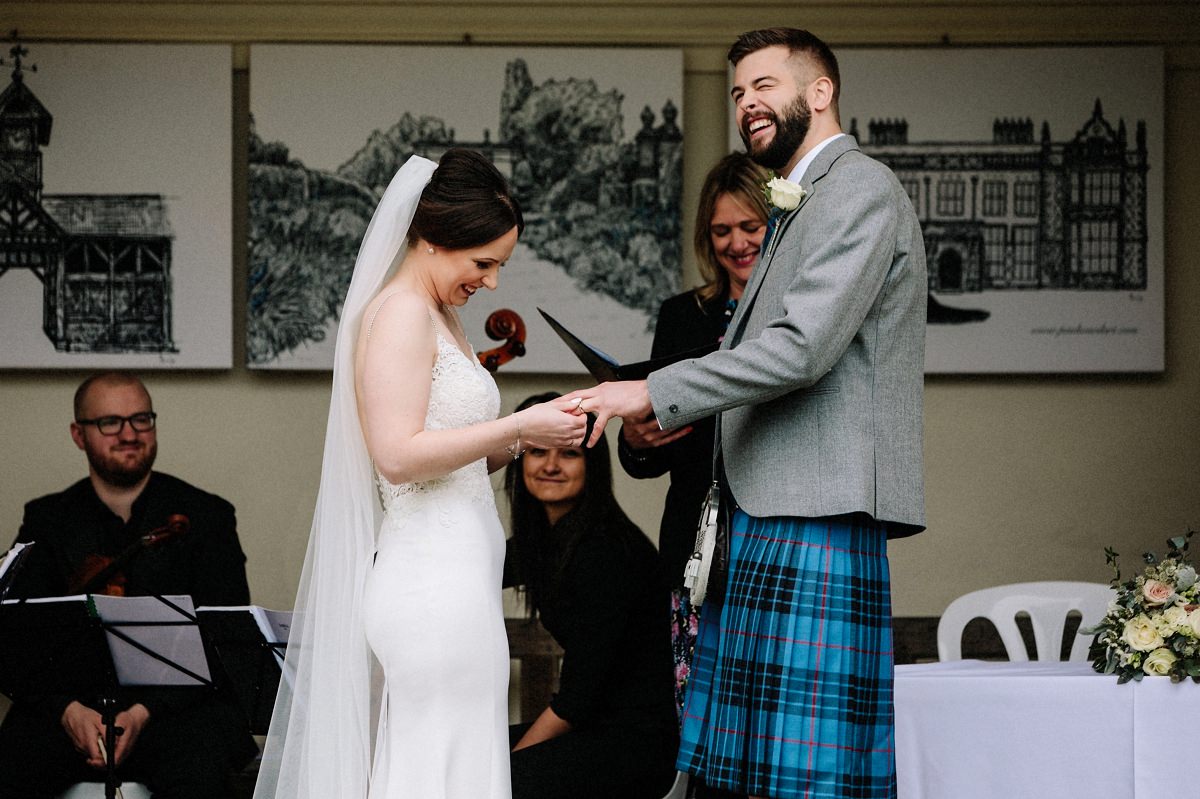 Bride laughing trying to put the wedding ring on the grooms finger