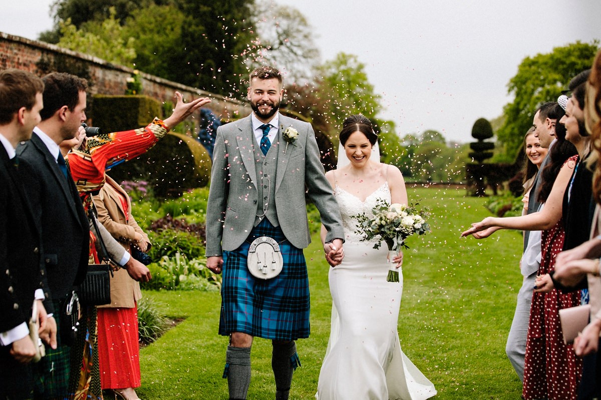 Bride and groom walking down the aisle getting showered with confetti at Arley Hall Gardens