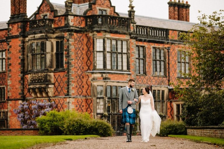 Bride and groom walking linking arms with the stunning Arley Hall in the background