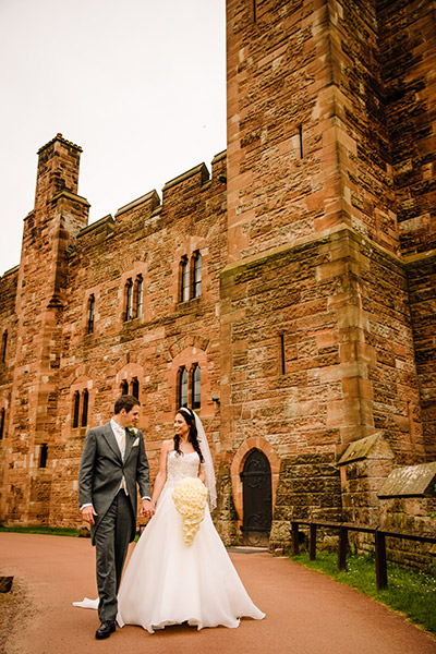 Bride and groom walking hand in hand in the grounds of peckforton castle