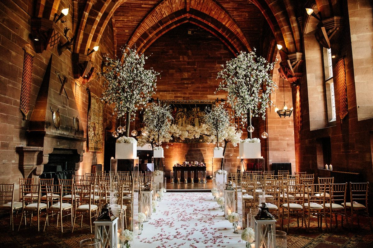 The Great Hall at Peckforton Castle dressed in floral displays and candles for the wedding ceremony