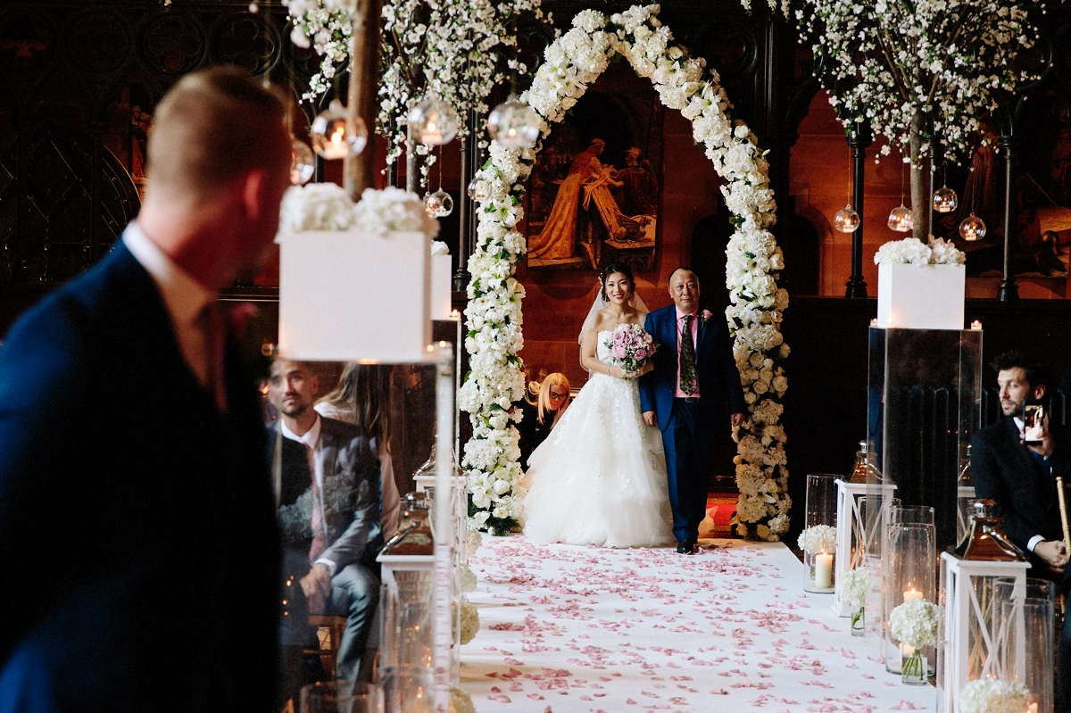 Bride walking down the aisle with her father with the groom looking on at Peckforton Castle