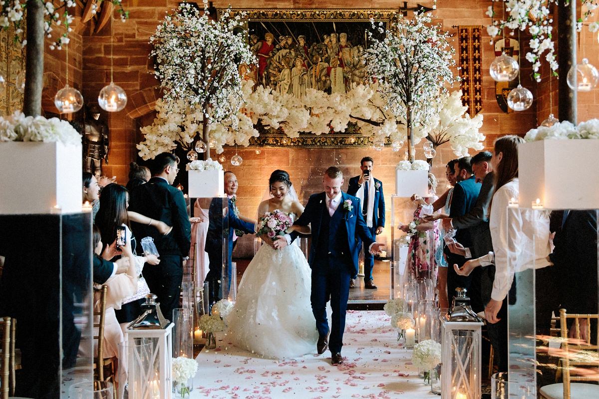 Bride and groom showered with confetti as they walk down the aisle at Peckforton Castle