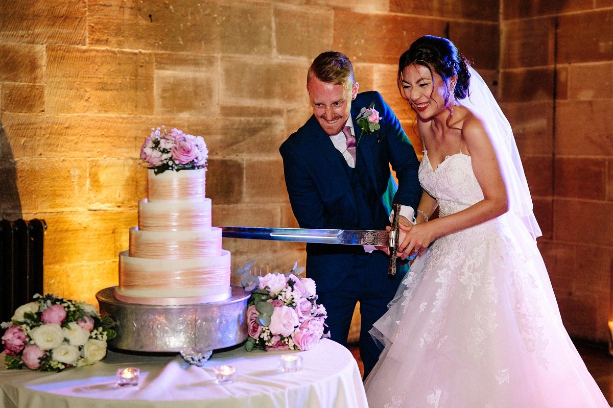 Bride and groom cutting the wedding cake with a sword at Peckforton Castle